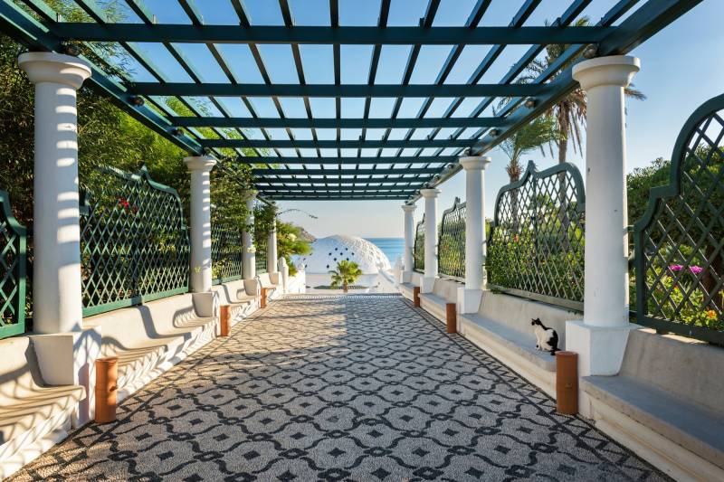 Papermoon Fototapete »PERGOLA-RHODOS BLUMEN SEE MEER TERRASSE PALMEN DÜNEN« von Papermoon